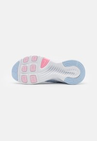 Semelle d'une chaussure de sport blanche avec des grips en caoutchouc roses et bleus et un logo Nike rose près de la voûte plantaire.