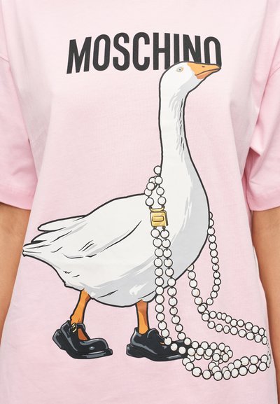 Ροζ βαμβακερό μπλουζάκι με γραφικό ενός λευκού χήνου που φοράει μαύρα παπούτσια, στολισμένο με μαργαριταρένιο κολιέ και το κείμενο "MOSCHINO" από πάνω.