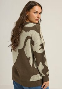 Sweter dzianinowy w odcieniach beżu i brązu, z motywem kamuflażu. Luźny krój, z prążkowanymi mankietami i dołem oraz okrągłym dekoltem.