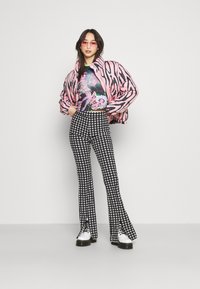 Giacca piumino a righe rosa e nere, top corto grafico con design floreale, pantaloni svasati a scacchi, e stivali bianchi con lacci.