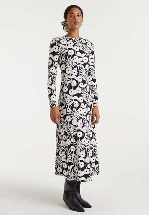 Vestido de manga larga en un patrón floral en blanco y negro, con corsé ajustado y falda acampanada, combinado con botas negras hasta el tobillo.