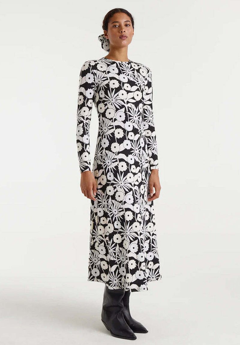 Vestido de manga larga en un patrón floral en blanco y negro, con corsé ajustado y falda acampanada, combinado con botas negras hasta el tobillo.