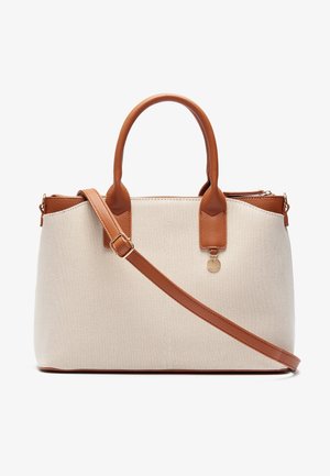 Bolso de tela beige con asas de cuero marrón y correa de hombro ajustable, con un pequeño charm dorado redondo cerca de la parte superior.