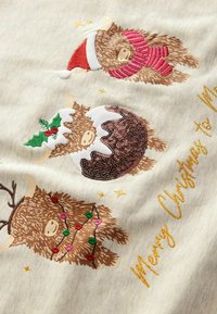 Tissu beige en coton présentant trois vaches des Highlands de style cartoon. Détails comprenant une écharpe rouge, un bonnet de Père Noël et un design chocolat menthe avec des ornements.