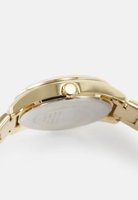 Guld-tone armbåndsur med rund urkasse, rustfrit stålarmbånd, glat bezel og sidekrone. Bagsiden er indgraveret med detaljer.