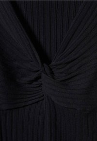 Tissu noir côtelé avec un détail de nœud torsadé au centre, créant une texture froncée et des lignes diagonales sur le matériau.