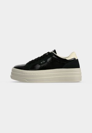 Zwarte lage sneaker met dikke gebroken witte zool, zwarte veters en "A|X" logo op de zijkant en hielkraag.