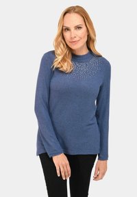 Langärmliger blauer Pullover mit rundem Ausschnitt und dekorativen Strasssteinen, die in einem strahlenden Muster über die Brustpartie angeordnet sind.