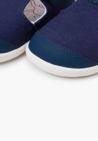 Zapatillas de lona azul marino con suelas de goma, con punta redondeada y diseño recortado. Acentuadas con una sección suave de color azul oscuro en la parte delantera.