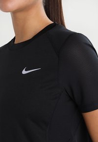 Camiseta deportiva negra con una tela suave y mangas de estructura de malla, con un logo blanco de Nike en el pecho.