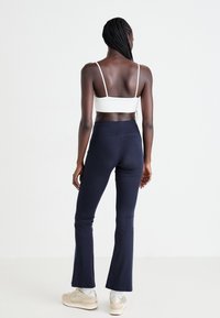 Marineblaue Schlagleggings kombiniert mit einem weißen, cropped Oberteil, das ein figurbetontes Design, eine glatte Textur und einen minimalistischen Schnitt aufweist.