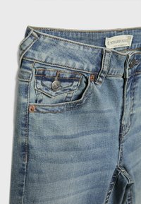 Lys blå denimjeans med mid-rise talje, fem lommer, subtil slitage og kobberfarvet hardware. Brandmærke synligt på taljebåndet.