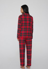 Conjunto de pijama de franela a cuadros rojos que presenta una camisa de botón con cuello y pantalones a juego, ambos con acentos en negro y verde en el patrón.