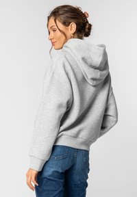 Grauer, oversized Kapuzenpullover aus weichem Material, ausgestattet mit einer Kordelzugkapuze und gerippten Bündchen, kombiniert mit blauen Jeans.