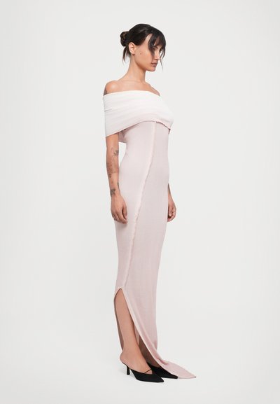 Rochie off-shoulder din țesătură roz deschis, cu un design mulat, slit lateral și o suprapunere texturată de culoare albă. Purtați cu tocuri negre.
