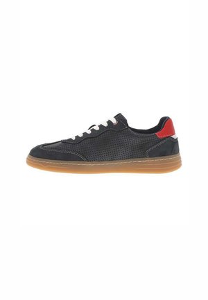 Sneaker en cuir perforé noir avec des lacets blancs, accent rouge au talon, semelle en caoutchouc beige et coutures le long des bords.
