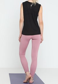 Mustaton hihaton paita, jossa on selkäosa, yhdistettynä vaaleanpunaisiin legginsseihin, joissa on tekstuurit yksityiskohdat nilkoissa.