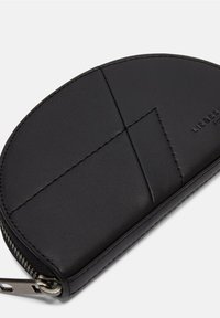 Portafoglio in pelle nera con forma arrotondata, caratterizzato da linee di design cucite e chiusura con zip. Sottile dettaglio del marchio in rilievo sulla superficie.