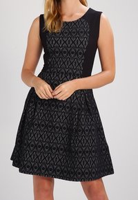 Svart klänning med en figurnära byst i en texturerad diamantdesign och en utställd kjol. Enkel design med ärmlös snitt.