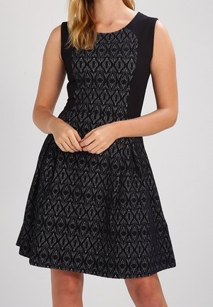 Zwarte jurk met een aangesloten bovenkant met een gestructureerd diamanten patroon en een uitlopende rok. Eenvoudig ontwerp met mouwloze snit.