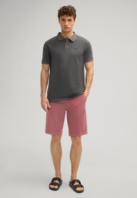 Polo grigio a maniche corte, logo sul petto; pantaloni corti rosa, orlo piatto; sandali neri. Trama liscia, vestibilità casual.