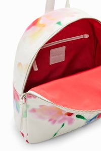 Sac à dos rond blanc avec un motif floral, doté d'un intérieur rouge, fermeture éclair et petite poche intérieure avec une étiquette de marque.