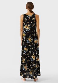 Vestido maxi en tejido ligero negro con un patrón floral en amarillo y azul. Presenta un escote de espalda y un diseño de falda devolante.