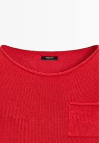 Maglione rosso lavorato a maglia con scollo rotondo e una piccola tasca rettangolare sulla parte destra del petto.