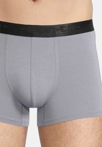 Gray fabric boxer briefs with a black elastic waistband featuring a logo. Smooth texture with a fitted design and short legs.