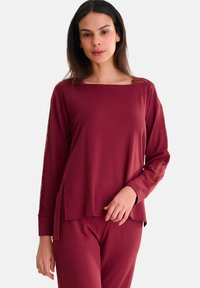 Haut bourgogne à manches longues avec des accents en dentelle le long des manches, présentant un décolleté large et des fentes latérales pour un ajustement décontracté.