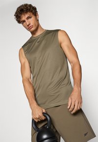 Olivegrünes ärmelloses Sportoberteil aus glattem, leichtem Material. Mit schwarzem Logo auf der Brust und kombiniert mit passenden Shorts.