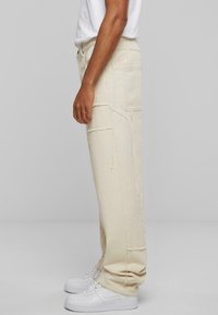 Beige bomullscargobukser med avslappet passform, med lapplommer og rå kantdetaljer, brukt sammen med hvite sneakers.