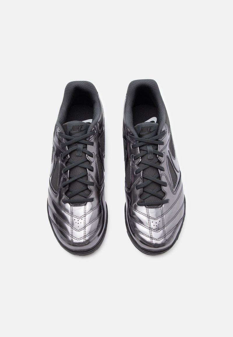 Schwarze Sportschuhe mit einer glänzenden, strukturierten Oberfläche. Zu den Merkmalen gehören schwarze Schnürsenkel, Netzpaneele und ein markantes geschwungenes Design.