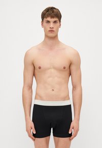 Schwarze Baumwoll-Boxershorts mit einem grauen elastischen Bund, der ein Logo trägt. Glatte Textur und figurbetontes Design. Keine Muster oder zusätzlichen Akzente.