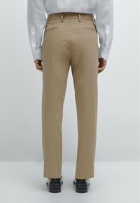 Pantaloni beige con vestibilità sartoriale, tasche laterali e due tasche posteriori. Realizzati in materiale liscio, abbinati a scarpe nere.