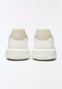 Fehér tornacipők bézs részletekkel, sima bőrfelsőrésszel, texturált kidolgozással és vastag talppal, lekerekített formával.