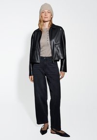 Black leather cropped jacket with two front pockets, paired with a light gray button-up sweater, dark jeans, and black flats. Textured beige beanie.