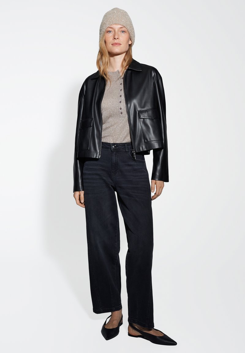 Black leather cropped jacket with two front pockets, paired with a light gray button-up sweater, dark jeans, and black flats. Textured beige beanie.