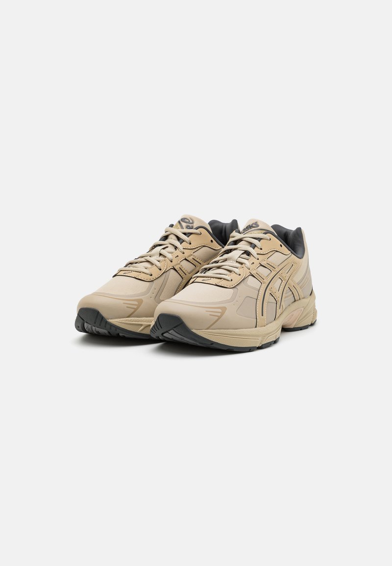 Baskets de sport beiges avec un dessus synthétique lisse, un embout renforcé, des accents noirs, un système de laçage et une semelle extérieure en caoutchouc texturé.
