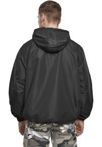 Svart huva jacka med en lös design, elastiska manschetter och en mjuk textur. Bärs med byxor i kamouflagemönster.