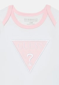 Body in cotone bianco con una targhetta triangolare rosa, ricamata con il logo "GUESS" e un punto interrogativo decorativo. Design morbido e a maniche corte.