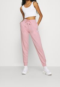 Pink sweatpants with elastic waistband and adjustable drawstring, paired with a white cropped tank top and white sneakers. Smooth texture.