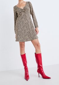 Robe imprimé léopard à manches longues et décolleté en V profond, associée à des bottes à talons aiguilles rouges brillantes montant jusqu'aux genoux avec fermeture éclair.