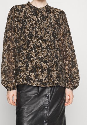 Femme portant un chemisier noir transparent à imprimé floral avec de longues manches bouffantes et une jupe en cuir noir boutonnée.