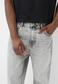 Faded grå denimjeans med rak passform, fem fickor och knäppning. Bärs med en svart t-shirt med kort ärm.