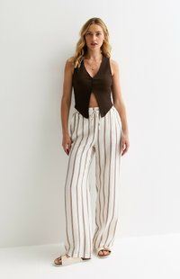 Top sans manches côtelé marron avec des boutons et un col en V, associé à un pantalon large rayé blanc avec des accents marron. Sandales plates montrées.