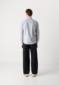 Lichtblauwe overhemd met lange mouwen, van achteren getoond. Donkere wijde broek en witte schoenen maken de outfit compleet.