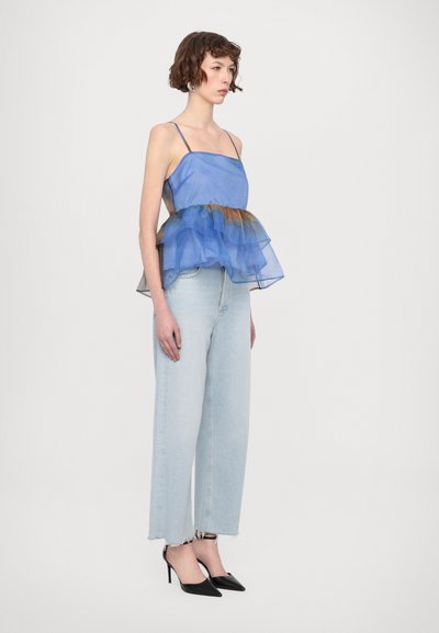Blå gjennomsiktig lagdelt topp med en volangkant, kombinert med lyseblå høytlivsjeans og svarte stiletthæler.