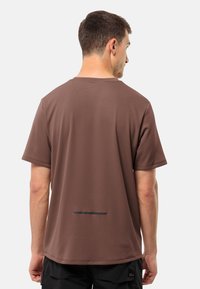 Brun kortærmet T-shirt lavet af glat, let stof. Har en vandret sort stribe på tværs af ryggen.