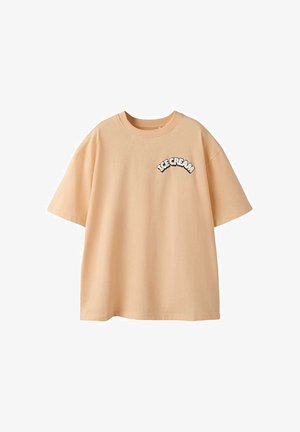T-shirt beige à manches courtes avec col rond et inscription graphique "ICE CREAM" en blanc et noir sur le côté gauche de la poitrine.